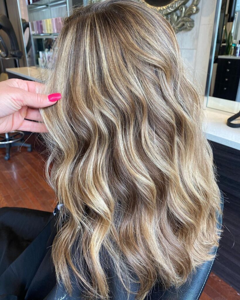 Back view of wavy hair colored with freehand balayage, showing a blend of blonde and caramel highlights.