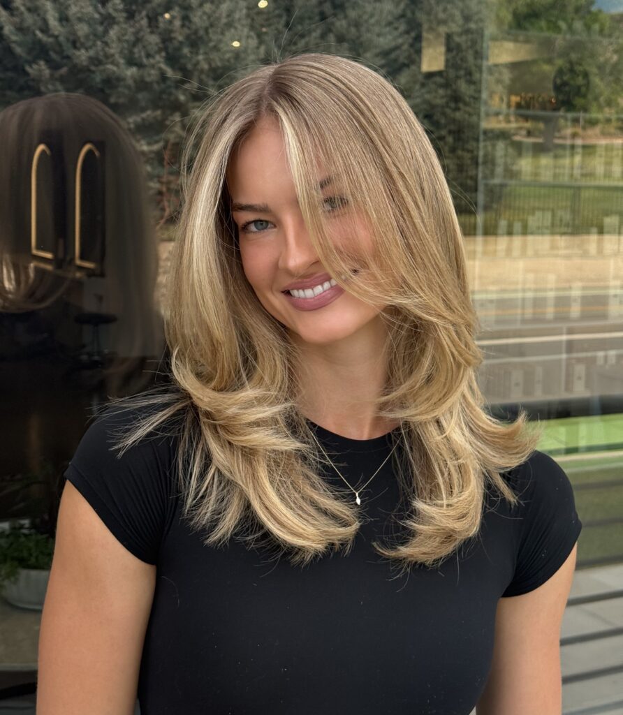 Layered blonde haircut with side‑swept bangs on a smiling woman.
